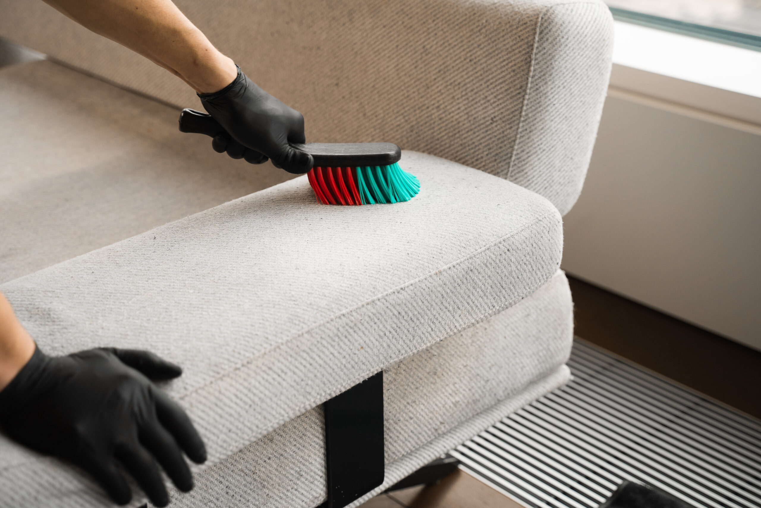 Cleaner is brushing off dust from the sofa at home. Removing dirt and stains from couch with dry-cleaning brush.